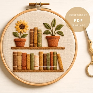 Op de afbeelding: Een borduurring met een boekenplankontwerp, inclusief potplanten en boeken. Het ontwerp bevat een zonnebloem en een plant met groene bladeren. De tekst "EMBROIDERY PDF TEMPLATE" is zichtbaar. Een gouden schaar bevindt zich aan de rechterkant.