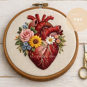 May include: Anatomy-themed embroidery art featuring a detailed human heart design, adorned with colorful floral accents. The embroidery is set within a wooden hoop, with the text "Embroidery PDF Pattern" visible. A pair of gold scissors rests nearby.