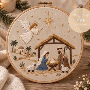 Könnte beinhalten: Ein runder Stickrahmen aus Holz mit einem Stoffeinsatz, der eine Krippenszene zeigt. Das Motiv umfasst einen Engel, einen Stern, einen Stall, Figuren und Schafe, mit dem Text EMBROIDERY PDF PATTERN in der oberen rechten Ecke.