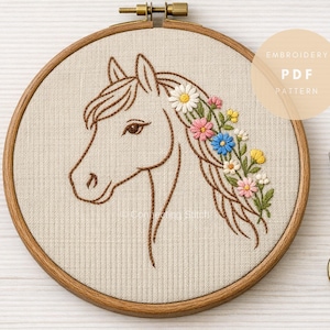 Może przedstawiać: Tamborek z wzorem głowy konia. Koń jest brązowy, z grzywą ozdobioną kolorowymi kwiatami. Tekst "EMBROIDERY PDF PATTERN" znajduje się w okręgu. Z prawej strony złote nożyczki.
