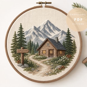 May include: An embroidery hoop containing a fabric panel with a stitched mountain landscape featuring a log cabin, tall pine trees, a winding path, and a wooden signpost. The text EMBROIDERY PDF PATTERN is visible in the upper right corner.