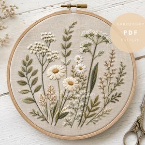 Op de afbeelding: Een borduurring met een bloemenontwerp met madeliefjes en andere wilde bloemen in crème, groen en bruin tinten. De tekst "EMBROIDERY PDF PATTERN" is zichtbaar. Een vintage schaar ligt ernaast.