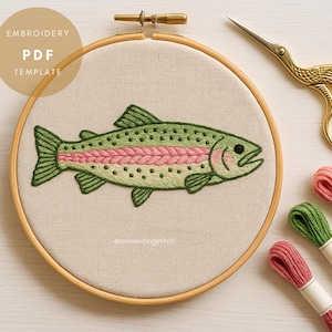 Puede incluir: Un bastidor de bordado con un diseño detallado de pez verde y rosa. El texto "EMBROIDERY PDF TEMPLATE" está en un círculo. Tijeras doradas y carretes de hilo en verde y rosa también son visibles.