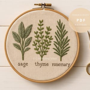 May include: Embroidered herbs of sage, thyme, and rosemary on a beige fabric within a wooden embroidery hoop. The green embroidery is detailed. The words "sage", "thyme", and "rosemary" are embroidered below each herb. A PDF pattern is available.