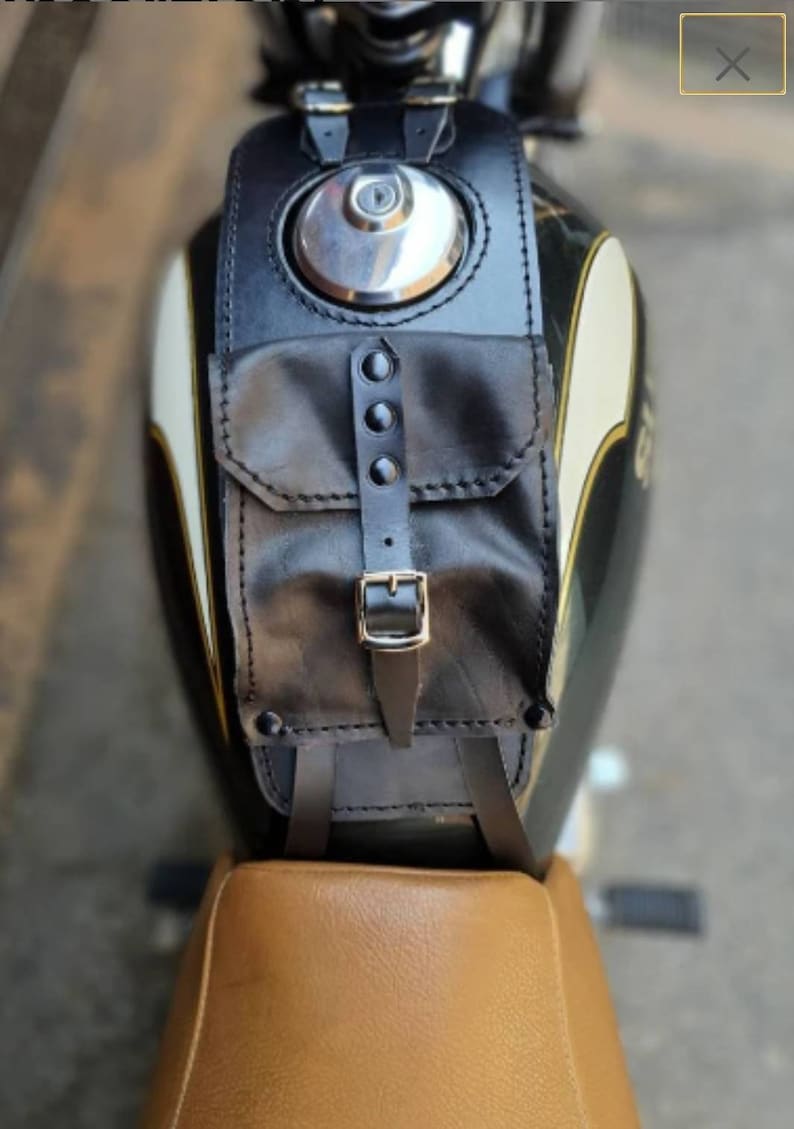 May include: Black leather motorcycle tank bag with a small pocket and a buckle closure. The bag is attached to a motorcycle with straps.