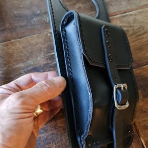 May include: Black leather motorcycle tank bag with a large circular opening and a smaller pocket with a buckle closure.