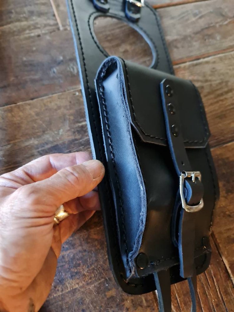 May include: Black leather motorcycle tank bag with a large circular opening and a smaller pocket with a buckle closure.