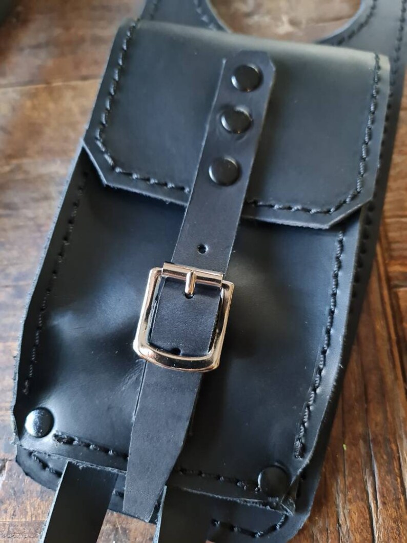 May include: Black leather pouch with a silver buckle and three black snaps. The pouch has a flap with a stitched edge.