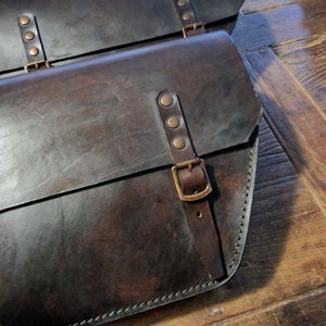 May include: Two brown leather motorcycle saddlebags with brass buckles and rivets.