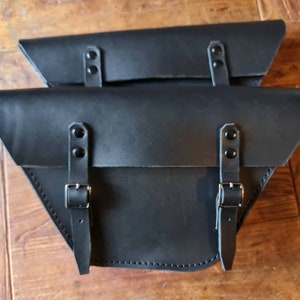 Könnte beinhalten: Zwei schwarze Leder-Motorradsatteltaschen mit Schnallen und Riemen.