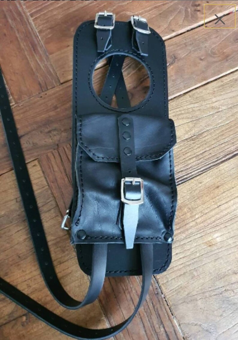 May include: Black leather motorcycle tank bag with a large pocket and adjustable straps. The bag has a circular opening and silver buckles.