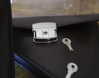 May include: A brown leather portfolio with a silver clasp and two silver keys. The portfolio has a flap that closes with the clasp.