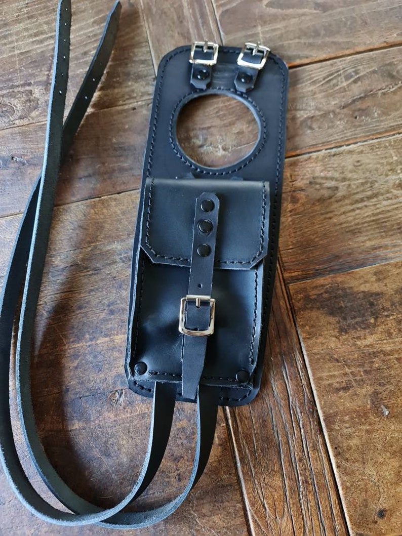May include: Black leather motorcycle tank bag with a small pocket and two straps. The bag has a buckle closure and a circular opening.