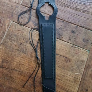 Peut inclure: Couvre-réservoir en cuir noir avec une découpe en forme de croix et un design cousu. Le couvre-réservoir a une longue sangle avec une boucle à l'extrémité.