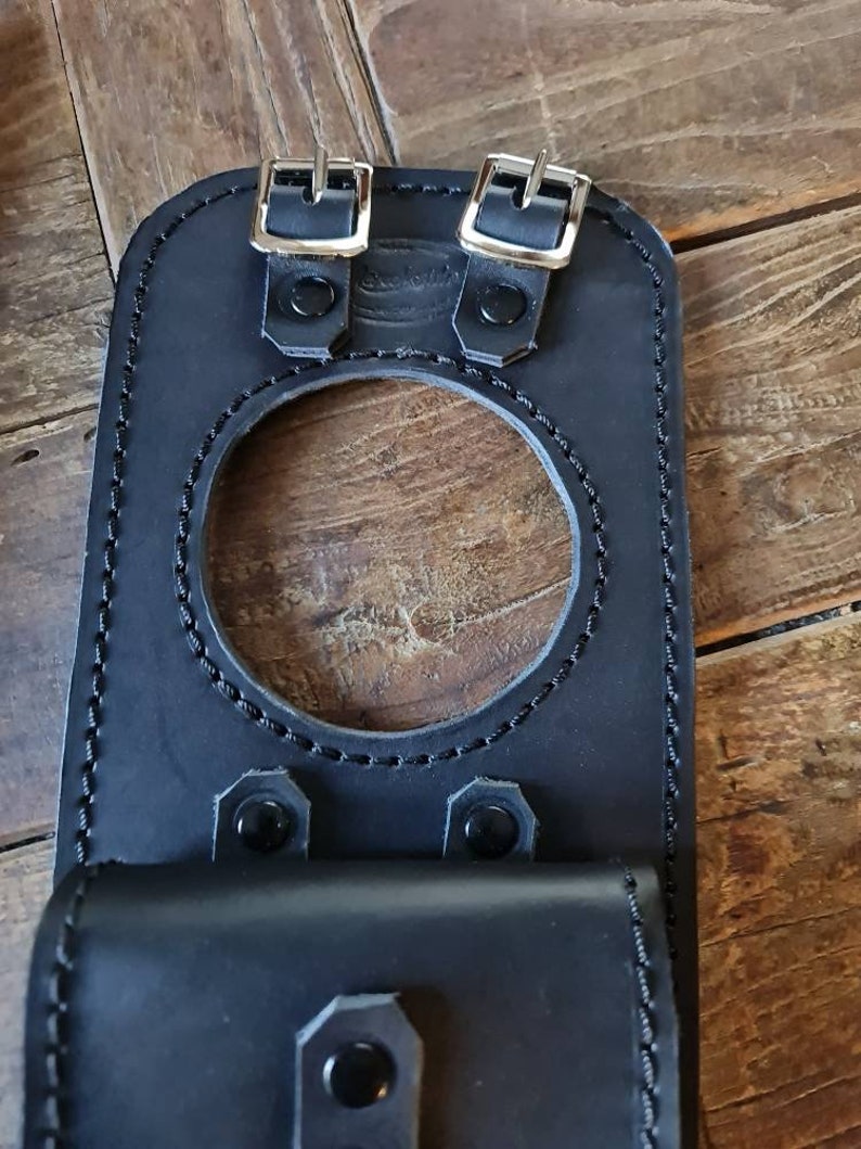 May include: Black leather motorcycle gas tank bag with two buckles and a flap. The bag has a circular opening for the gas cap.