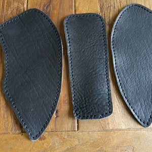 Peut inclure: Trois patchs en cuir noir avec des bords cousus. Les patchs ont la forme d'une larme et une surface texturée.