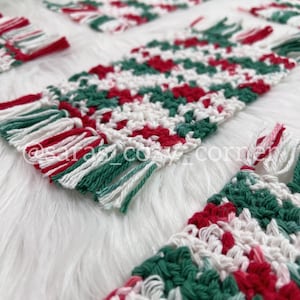Puede incluir: Conjunto de cuatro posavasos de ganchillo con un patrón de rayas rojas, blancas y verdes. Cada posavasos tiene un borde de flecos.