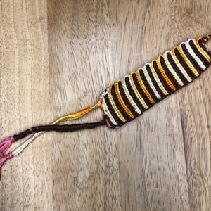 May include: A brown, white, and yellow striped friendship bracelet with pink tassels.