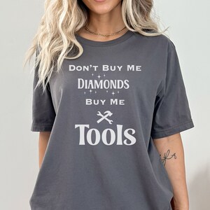 Puede incluir: Camiseta gris con el texto "No me compres diamantes, c&oacute;mprame herramientas" y un gr&aacute;fico blanco de llave inglesa y martillo.
