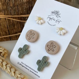 May include: A selection of handmade stud earrings displayed on a white card. The earrings showcase daisy, sand dollar, and cactus designs in white, tan, and green. The card includes the text "Forget me Knot Handmade Shop" and social media details.