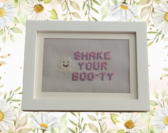 Puede incluir: Un bordado de punto de cruz enmarcado en blanco con un sol amarillo sonriente y el texto "Shake Your Booty" en rosa.