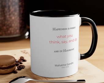 May include: White ceramic mug with a black interior and handle. The mug features the quote "Happiness is when what you think, say, and do are in Harmony" attributed to Mahatma Gandhi.
