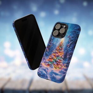 May include: Two phone cases with a winter forest scene. One case is black, the other has a blue background with a Christmas tree covered in colorful lights. Snow covers the ground and the trees.