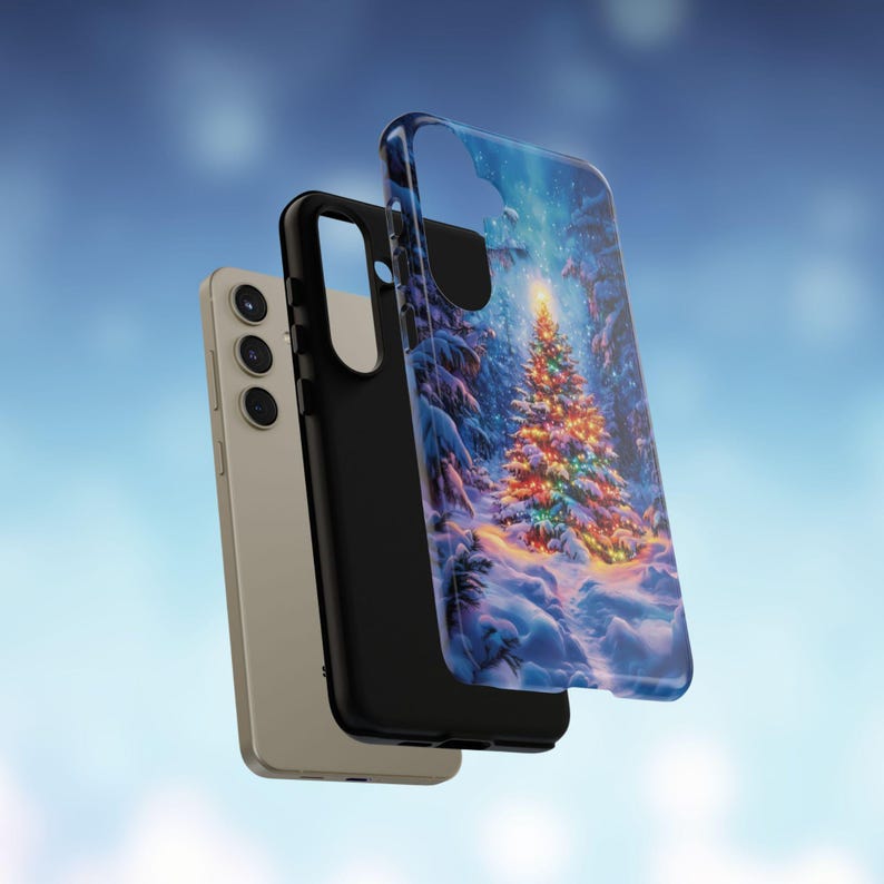 May include: A smartphone and two phone cases. One case features a winter scene with a decorated Christmas tree. The other case is black. The phone is a light gold color.