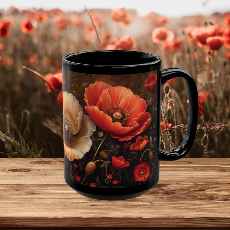 May include: Black ceramic mug with a floral design featuring red and white poppies on a dark background. The mug is sitting on a wooden surface.