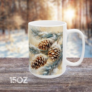 Peut inclure: Mug en c&eacute;ramique blanche avec une sc&egrave;ne d'hiver repr&eacute;sentant des branches de pin avec de la neige et des pommes de pin. La tasse est de 15 oz.