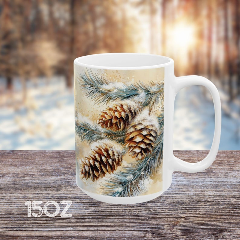 Peut inclure: Mug en c&eacute;ramique blanche avec une sc&egrave;ne d'hiver repr&eacute;sentant des branches de pin avec de la neige et des pommes de pin. La tasse est de 15 oz.