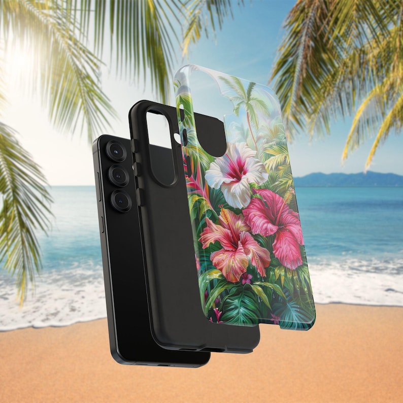 May include: A black smartphone and two phone cases. One case is black, and the other is clear with a tropical floral design featuring pink and white hibiscus flowers, green leaves, and palm trees. The background shows a beach scene.