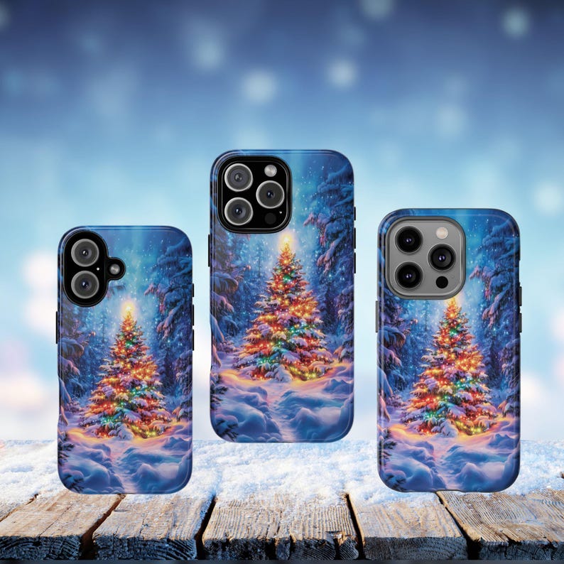 May include: Three phone cases with a winter forest scene featuring a decorated Christmas tree. The cases have a blue background with a snowy landscape and a brightly lit tree. The cases are on a wooden surface.