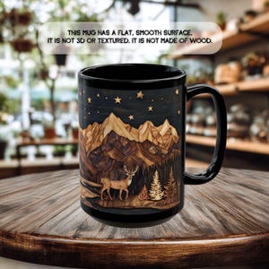 May include: A black ceramic mug featuring a printed graphic of a deer standing in a forest before mountain peaks under a starry night sky. The text on the mug reads: THIS MUG HAS A FLAT, SMOOTH SURFACE, IT IS NOT 3D OR TEXTURED. IT IS NOT MADE OF WOOD.