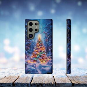 May include: A phone case featuring a winter forest scene with a decorated Christmas tree. The case is blue with a snowy landscape and a brightly lit tree. The side view shows a black case with buttons.