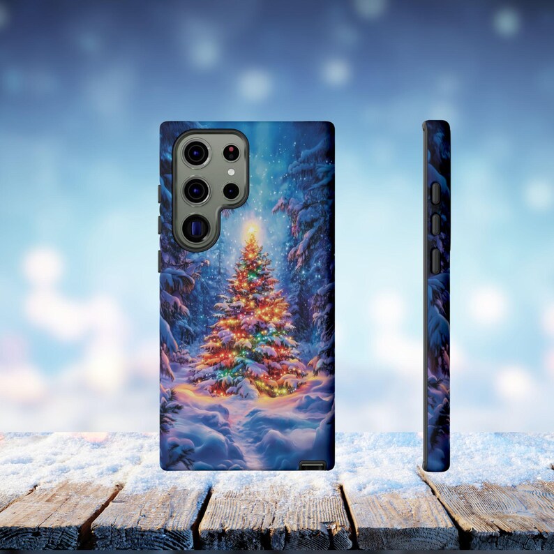 May include: A phone case featuring a winter forest scene with a decorated Christmas tree. The case is blue with a snowy landscape and a brightly lit tree. The side view shows a black case with buttons.