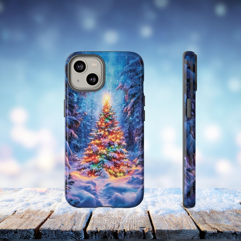 May include: A phone case featuring a winter forest scene with a decorated Christmas tree. The case has a blue background with falling snow and a wooden table in the foreground. The side of the case is also visible.