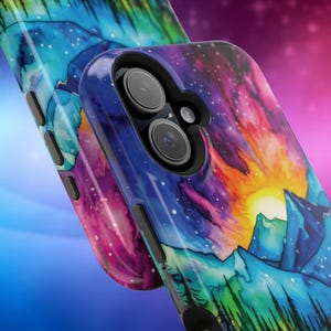 May include: A phone case featuring a watercolour design of a mountain range and a starry sky. The case is blue, purple, green, and orange. The phone case has a cutout for the camera lens.