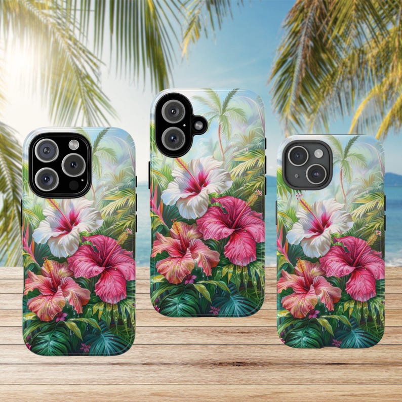 May include: Three phone cases with a tropical floral design featuring hibiscus flowers in shades of pink and white, set against a backdrop of palm trees and a blue sky. The cases are on a wooden surface.