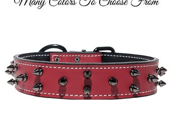 Puede incluir: Un collar de cuero rojo con dos filas de púas de metal gris, costuras blancas en contraste y una hebilla negra. El texto "Many Colors To Choose From", "Red Genuine Leather Gunmetal Spikes" y "PIT BULL GEAR" es visible en la imagen.