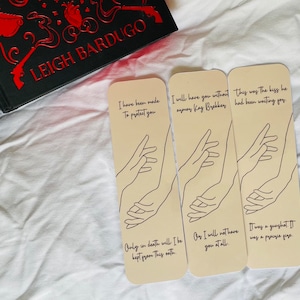 Puede incluir: Tres marcapáginas beige con texto negro y un dibujo de línea de dos manos. El texto en los marcapáginas dice "I have been made to protect you", "Only in death will I be kept from this oath", "I will have you without any more Kay Byekkey", "Oy I will not have you at all", "This was the kiss he had been waiting for", "It was a gunshot. It was a promise given."