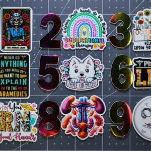 May include: A collection of colorful stickers and metallic numbers. Stickers include a skeleton nurse, a rainbow with "Occupational Therapy", a dog with "Take Ur Meds!", and a pharmacy design. Numbers 1-9 are also present.