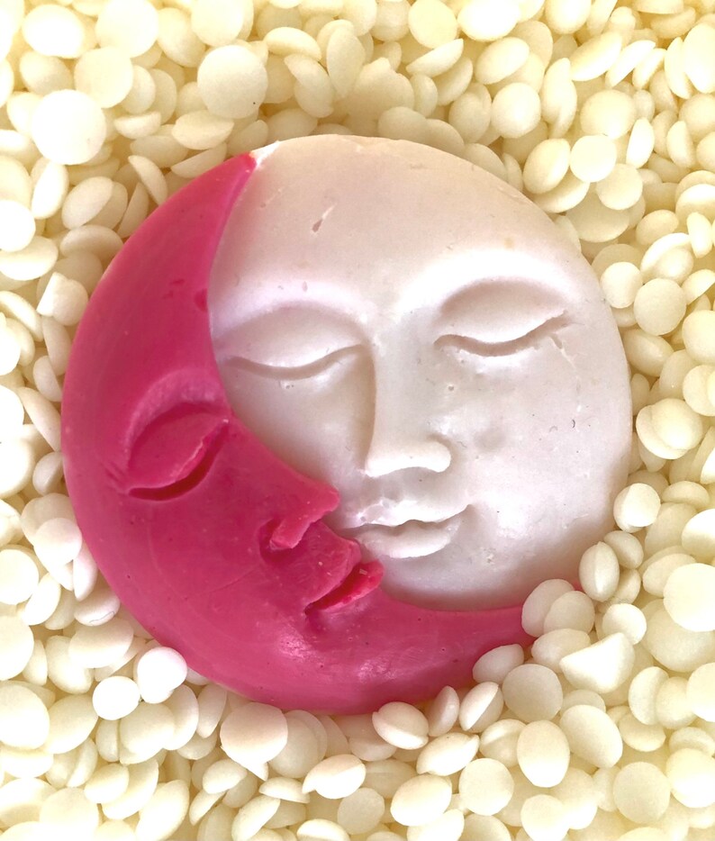 K&ouml;nnte beinhalten: Eine rosa und wei&szlig;e, sichelf&ouml;rmige Seife mit einem Gesicht darauf. Die Seife ist von wei&szlig;en Wachsflocken umgeben.