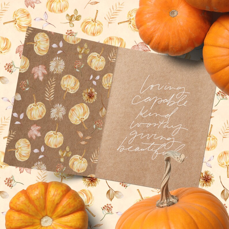 May include: A card with a brown background and white text that reads "loving, capable, kind, worthy, giving, beautiful." The card is surrounded by small watercolor pumpkins and leaves on a cream background.