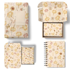 May include: Four different packaging options featuring a fall-themed pattern with watercolor pumpkins, leaves, and floral elements on a beige background. The pattern is repeated on a gift box, a notebook, a small gift box, and a gift wrap.