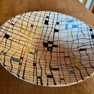 May include: A white ceramic bowl with a black and white grid pattern and colorful accents. The bowl has a slightly curved shape and a smooth, glossy finish.
