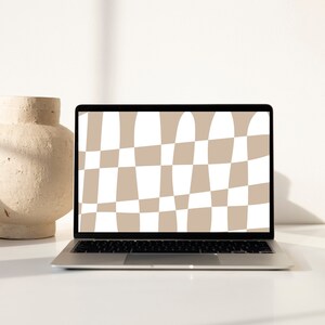 May include: A silver laptop displays a tan and white checkered pattern on its screen. A beige ceramic vase sits to the left of the laptop. The laptop is on a white surface, with a white wall in the background.