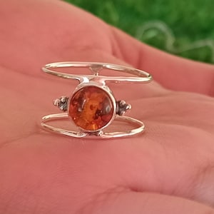 May include: A silver ring featuring a round amber stone set in the centre. The ring has a double band design with small silver accents on either side of the stone.