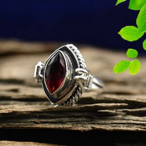 May include: A sterling silver ring featuring a marquise-cut, deep red gemstone. The ring has a detailed, textured band with a braided design and decorative accents on the sides. The gemstone is set in a bezel setting.