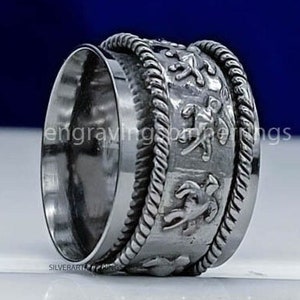 May include: A silver spinning ring with a textured band and intricate designs. The ring is made of metal and has a smooth, polished finish.